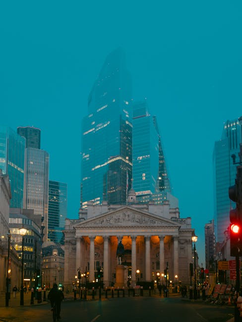 A historic, ornate stone building with large arched windows and detailed sculptures on the upper corners, situated on a city street with traffic lights and bollards in the foreground. The building has classic architectural features, including decorative stone carvings and columns. The surrounding environment includes modern high-rise structures in the background, and the street is lined with pavement and roadside markings. This setting suggests a central urban area suitable for house removals or furniture transport services. Man with Van Millbank, a professional removal company, may utilize such locations for loading or unloading during home relocation or furniture moving tasks, emphasizing efficient logistics and precise site handling.